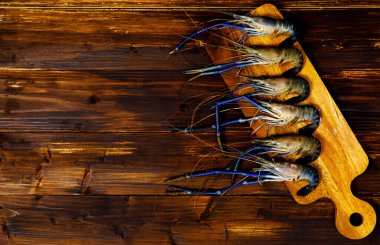 Yakın çekimde çiğ taze lezzetli lezzetli malzeme lezzetli büyük nehir kaplan karidesleri kesme tahtasında mavi pençeler ile süslenmiş siyah ahşap masa üzerinde boş metin alanı ile.