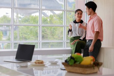 Asyalı, genç, mutlu koca ve güzel eş aşıkları gülümsüyor. Dışarıya bakıp, bilgisayar tezahüratları yapıyor ve oturma odasındaki cam pencerelerin yanında birlikte espresso içiyorlar..