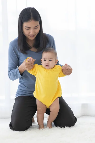 Asian mom is leader hand to teach her baby child to walking mom are smile and look happy with lovely to her baby child in bedroom with bright light in the morning is background.