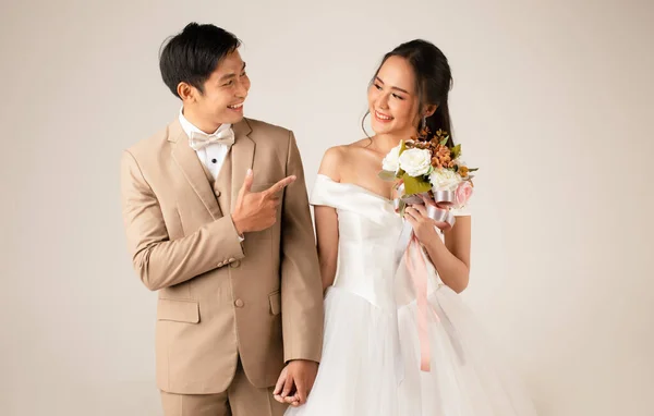 若い魅力的なアジアのカップル 男性はベージュのスーツを着て 女性は白いウェディングドレスを一緒に手を保持立っている 結婚式前の写真のコンセプト — ストック写真
