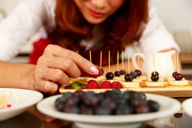 Ev hanımı lezzetli, sağlıklı, küçük, karışık meyveli, muzlu, böğürtlenli ve vişneli krep aperatifleriyle süslenmiş çubukla süsleme ve süsleme yapar.