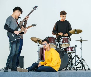 Birlikte müzik çalan genç müzisyenlerin grup fotoğrafı. Arkadaşlar enstrüman çalarken, sarı günlük kıyafetlerle oturan ve kameraya bakan genç çocuk. Ergenlik ilişkisi kavramı