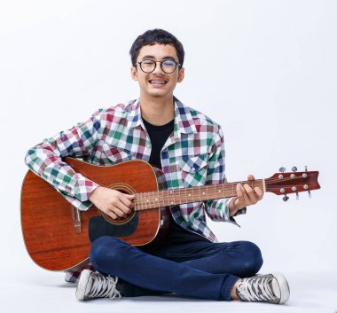 Akustik gitar tutan sevimli, gülümseyen genç bir gencin portresi. Profesyonel gitarist beyaz arka planda kameraya bakarken enstrüman çalıyor.