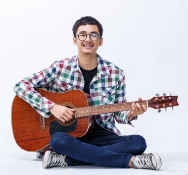 Portrait shot of a cute smiling young male teenager holding the acoustic guitar. Professional junior guitarist sitting and playing an instrument while looking at camera isolated white background clipart