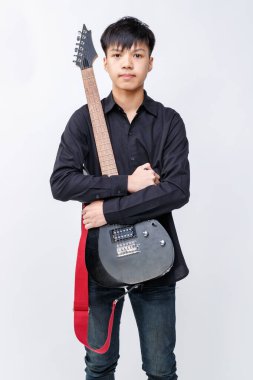Full-body portrait shot of an attractive young teenage musician holding an electric guitar on the ground in studio. Young junior guitarist looking at camera isolated with white background clipart