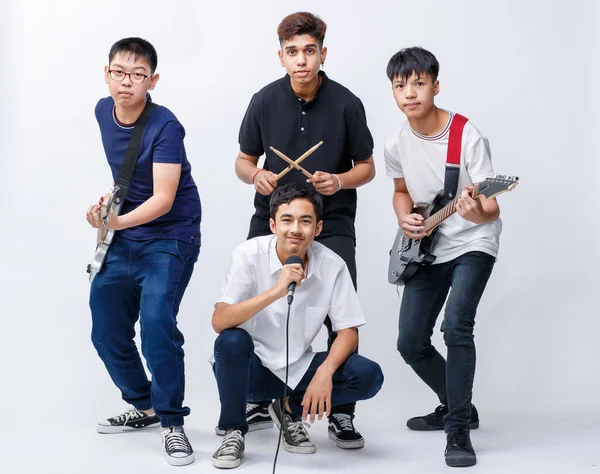 Bir enstrüman tutan ve beyaz arka planda izole edilmiş kameraya bakan dört genç müzisyenin portre çekimi. Genç gitarist, basçı, vokalist ve davulcunun grup fotoğrafı.