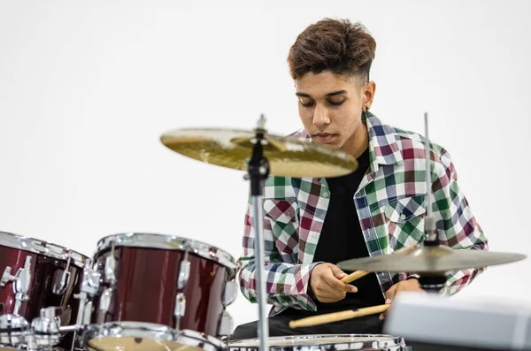 Front view portrait shot of teenage drummer playing the music. Young musician playing the drum while looking at the camera and smiling. Junior student playing an instrument with white background