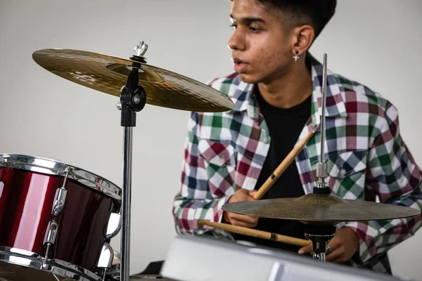 Close-up portrait shot of a teenage drummer playing the music. Selective focus at the drum with a drummer isolated on white background. Professional junior student playing an instrument as hobby