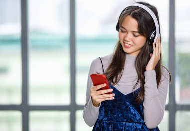 Genç Taylandlı bir gencin kulaklık ve akıllı telefonuyla müzik dinlerken çekilmiş portresi. Ellerinle müzik dinlemekten hoşlanan kız cep telefonu çalarken kulaklığa dokun.