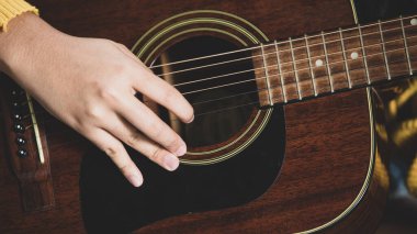 Genç müzisyen ellerinin akustik gitar çalarkenki yakın çekimi. Gitaristin ellerine odaklan. Gitarist evde müzik çalıyor..