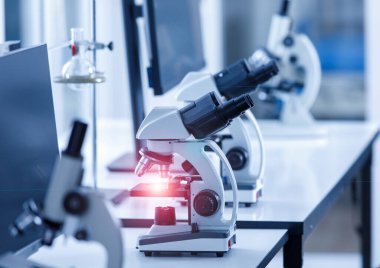 Laboratuvar çalışma masasında kırmızı ışık ve cam levha örneğiyle birlikte Coronavirus covid 19 'u izlemek için kullanılan iki göz görüşlü bilimsel mikroskop cihazının yakın çekim görüntüsü..