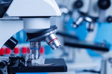 Bilimsel mikroskop büyütme merceğinin yakın plan görüntüsü cam plaka numunesinde hastane laboratuarındaki bulanık kırmızı ve mavi test tüplerinin önünde görüntüleniyor..