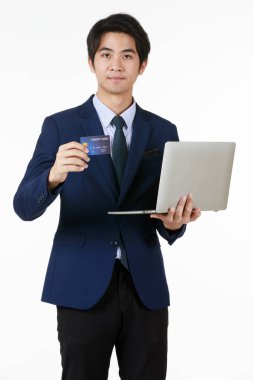 Resmi takım elbiseli genç Asyalı bir elinde dizüstü bilgisayarla diğer elinde kameraya bakan bir kredi kartı var. Mali ve yatırım türleri için uygun kişilik