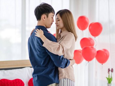 Sevgililer Günü 'nde romantik bir randevu sırasında ışık odasında gözleri kapalı dans eden Asyalı erkek ve kadının yan görüntüsü