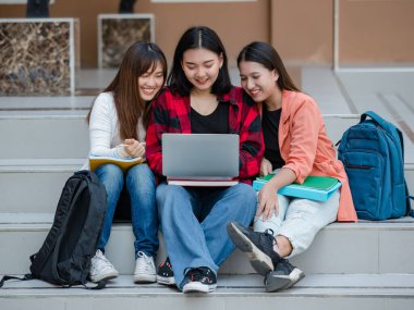 Üç çekici Asyalı kız üniversite öğrencisinden oluşan bir grup dışarıda üniversite kampüsünde dizüstü bilgisayar kullanarak birlikte çalışıyorlar. Eğitim, arkadaşlık ve üniversite öğrencilerinin hayatı kavramı.