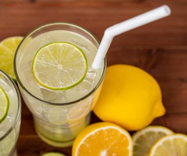 Ahşap masada taze limon ve limonla süslenmiş, saman, limon ve limon suyu ile serinletici iki bardak soğuk meyve suyu yakın plan fotoğrafı. Ferahlatıcı kavram.