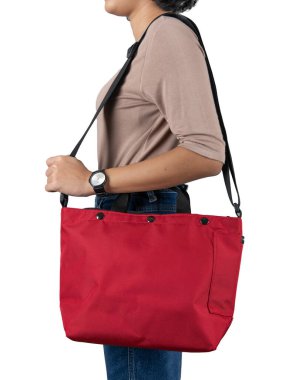 Uzun kollu kahverengi gömlekli ve kotlu bir kadın modelin izole edilmiş yakın çekim stüdyo fotoğrafı beyaz arka planda büyük kırmızı, çok amaçlı uniseks seyahat eden spor çantasından asılı duruyor..