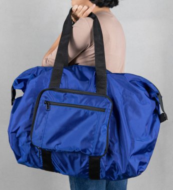 Kahverengi uzun kollu gömlekli ve kot pantolonlu kadın modelin yakın çekim stüdyo resmi gri arka planı önünde uzun omuz askısı olan, modaya uygun, büyük gri, uniseks çantasının sapını tutuyor..