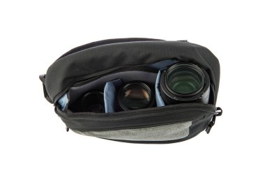 Profesyonel fotoğrafçının, su geçirmez, modaya uygun siyah kumaşlı orta boy sırt çantasının, beyaz arka plandaki yumuşak bölmenin içinde kamera ve lens tutarken çekilmiş yakın çekim görüntüleri..