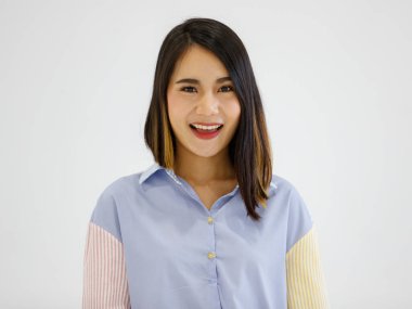 Mutlu bir Asyalı kadın resmi. Gri duvar arkasında yalnız poz veriyor. Dost canlısı, pozitif bir yüzü var..