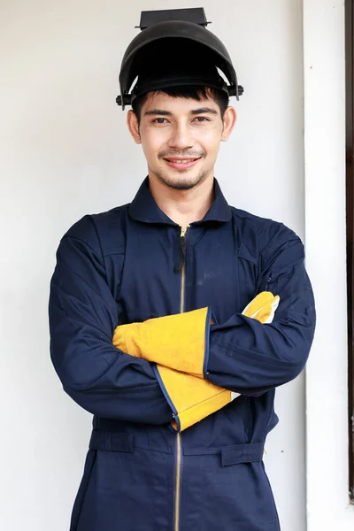 A young man in a mechanic\'s uniform with safety equipment such as a spark mask, fire protection yellow gloves. This is a good example of protection at work
