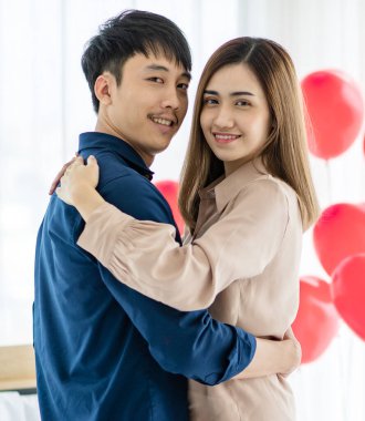 Sevgililer Günü 'nde romantik bir randevu sırasında Asyalı kadın ve erkeğin dans edişinin ve ışık odasında kameraya bakışımızın yan görüntüsü.