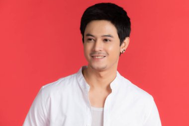 Beyaz tişörtlü yakışıklı Asyalı adamın portresi kırmızı arka planda izole edilmiş bir reklam fikri içinde rahat bir tatil için poz veriyor..