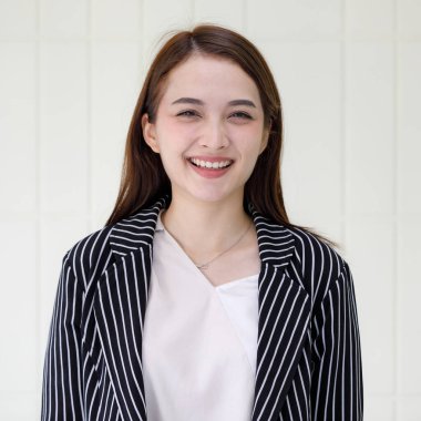 Uzun saçlı, güzel Asyalı bir iş kadınının, şık bir elbise giyip stüdyoda beyaz arka planda kameraya gülümserken yarı vücut pozu..