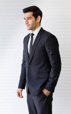 Beyaz arka planla izole edilmiş elleri cebinde, düzgün koyu takım elbiseli, orta yaşlı beyaz yakışıklı iş adamının yan görünümü. Mükemmel bir saç stiliyle çok güzel gülümsüyor.