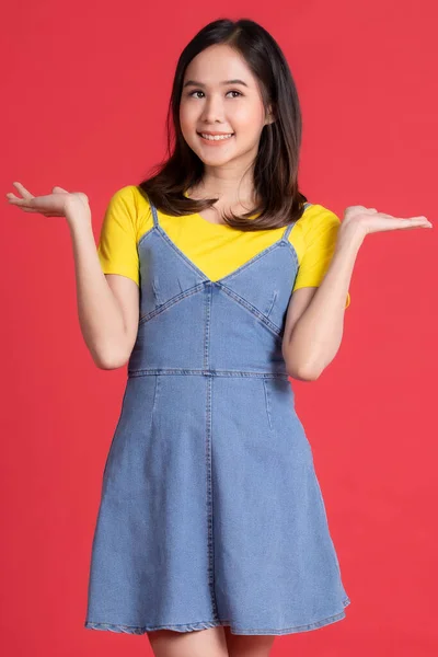 アジアの女の子赤い背景に優しい笑顔で商品やコンテンツジェスチャーを広告やプレゼンテーションで黄色のシャツと短いスカートポーズを身に着けています — ストック写真