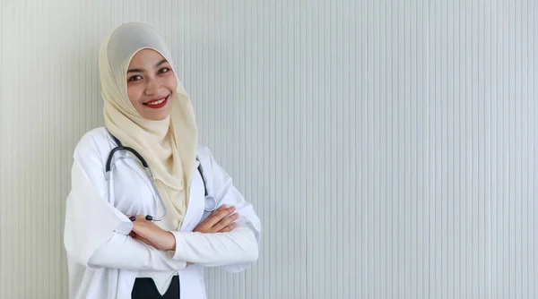 在灰色条纹背景下 积极的年轻穆斯林女医生交叉着双臂 对着相机微笑的画像 — 图库照片