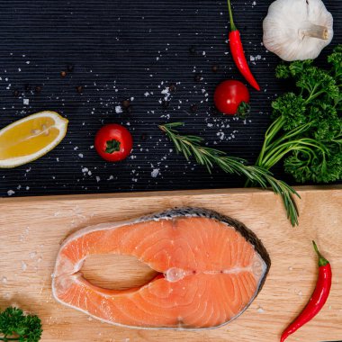 Taze çiğ somon balığı filetosunun foto fotoğrafı. İçinde pişirme malzemeleri, otlar ve siyah arka planda limon var.