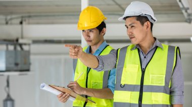 Sarı yansıtıcı yelek giyen ve güvenlik kaskı takan iki mühendis, savaş alanında birlikte çalışıyorlar..