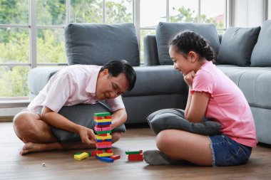 Mutlu kızı olan neşeli, genç Asyalı bir adam kanepenin yanında oturuyor ve hafta sonu evde kule oyunu oynuyor.