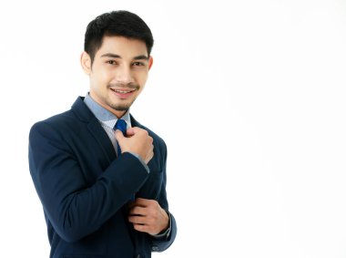 Gülümseyen yakışıklı genç Asyalı iş adamı kravatını izole beyaz arka plana göre ayarlıyor. Stüdyo yarı vücut portresi, iş ve başarı konsepti