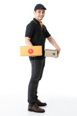 Neşeli Asyalı teslimatçı her iki elinde paketler tutuyor, kameraya gülümsüyor. İzole edilmiş beyaz arka planda siyah üniformalı kurye portresi. E-ticaret iş konsepti