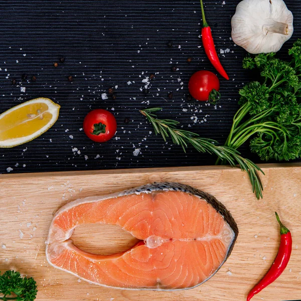 Taze çiğ somon balığı filetosunun foto fotoğrafı. İçinde pişirme malzemeleri, otlar ve siyah arka planda limon var.