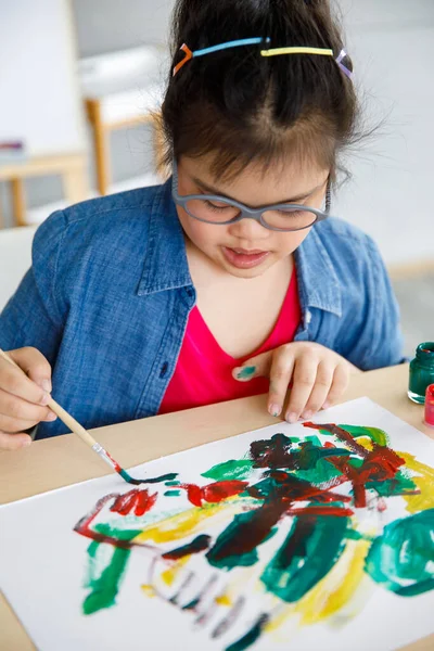 High angle of creative Asian girl with Down syndrome painting abstract picture during art lesson. Special education for disable child.