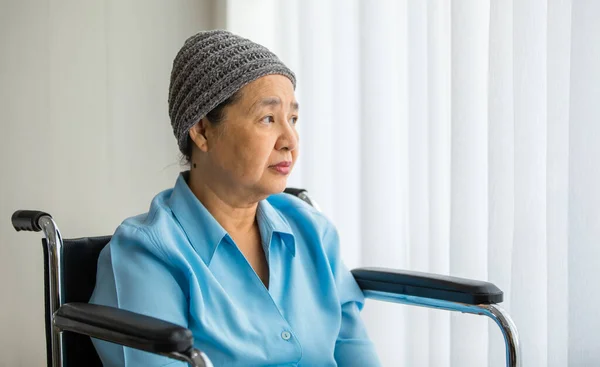 高齢のアジアの女性患者は 癌治療の化学療法の服効果で頭を覆った孤独な車椅子に座って 誰かが彼女を訪問するのを待つ — ストック写真
