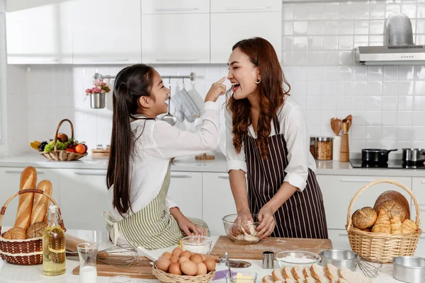 Asian Mother and daughter happily bake. The daughter teased her mother to bring the powder on her face at the kitchen in the house