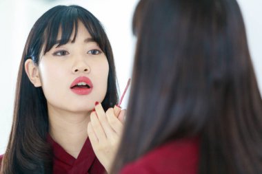 Çekici, genç, düz saçlı, sıradan kırmızı elbiseli ve dudaklarını rujla boyayan Asyalı bir kadının yatay portresi. Kadın yüzüne makyaj yapmış.