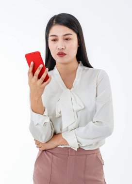 Asyalı güzel bir iş kadını, beyaz resmi gömlek ve pantolon giyiyor, özgüvenle gülümsüyor, ayakta duruyor, iletişim için kırmızı cep telefonunu tutuyor ve izole edilmiş beyaz arka planla bağlantı kuruyor.