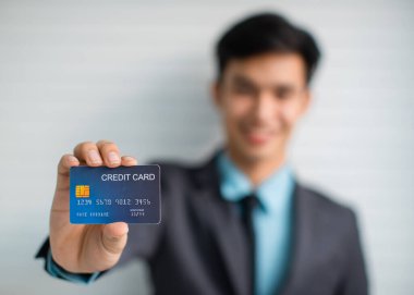 Banka hizmetlerinin gri arka planda reklamını yaparken kredi kartı gösteren erkek girişimcinin yumuşak odak noktası