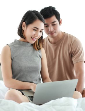 Yatakta birlikte oturan sevimli gülümseyen Asyalı aşık çiftin portresi. Hafta sonları evde çalışmak için dijital dizüstü bilgisayar kullanan kadına odaklan. Koca karısını cesaretlendirir.