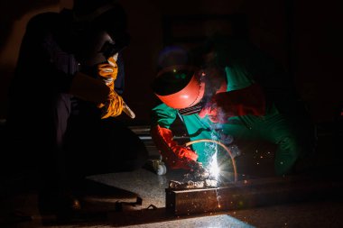 Tamirciler geceleri fabrikada fazla mesai yapmazlar. Tamirci tulumları, eldivenleri, botları ve metal kaynaklama kaskları olan güvenlik kıyafetleri giyen mühendisler..