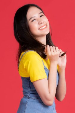 Asyalı kız, sarı tişört ve kısa etek giyip kırmızı arka planda gülen arkadaşça bir gülümsemeyle mal ve içerik sunumu yapıyor.