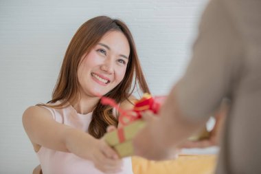 Uzun kolsuz elbise giyen Asyalı uzun kahverengi saçlı genç bir kadın erkek arkadaşından kırmızı kurdeleli hediye kutusunu aldı..