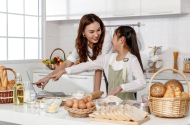 Asyalı anne ve kız, evdeki modern tarzda mutfaktaki internet bilgisayarından pişirme tarifleri üzerinde çalışmaya yardım ediyorlar.