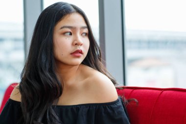 Siyah elbiseli, güzel, gülümseyen genç bir kızın, kanepede oturup stüdyodaki kameraya bakarken ön manzara portresi. Balo partisindeki güzel ergen kız.