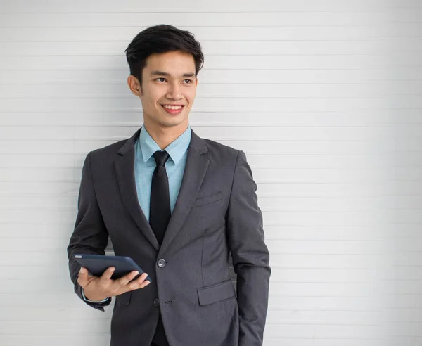 若いですアジアの男性マネージャーとともに現代的なタブレット笑顔と離れて見ながら立って近くグレーの壁 — ストック写真